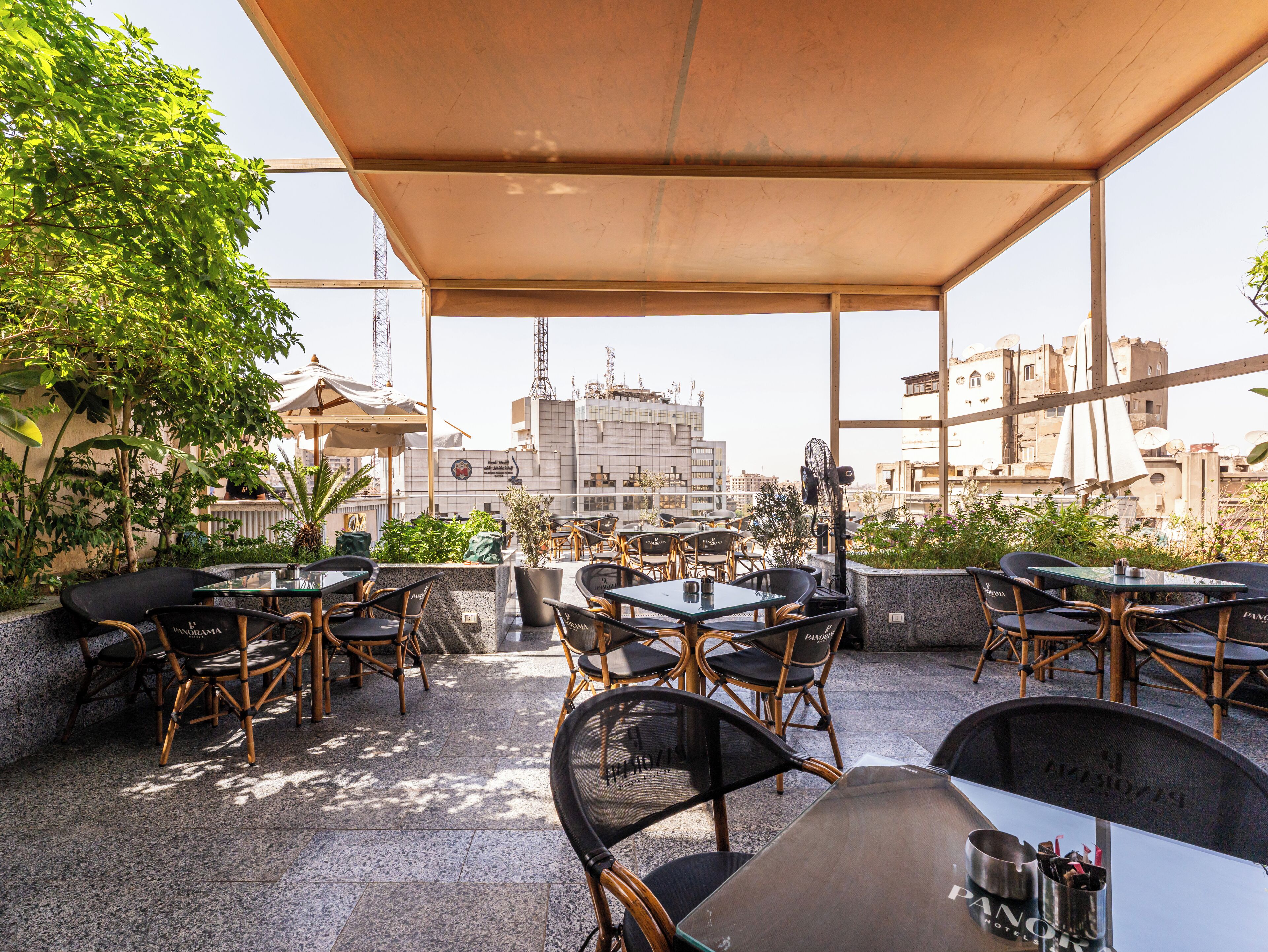 An outdoor patio with tables and chairs, a large umbrella, and a view of buildings in the background.