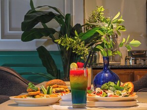 Une table avec de la nourriture, une boisson colorée et un vase bleu orné de verdure.