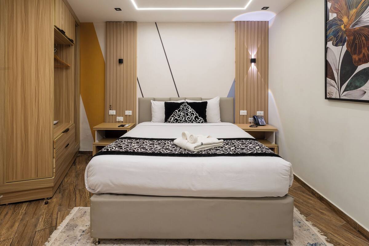Una habitación de hotel moderna con una cama grande, un armario de madera, mesitas de noche y un cuadro en la pared.