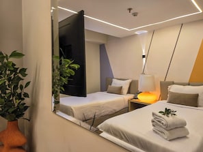 Une chambre d’hôtel avec deux lits, une table de chevet avec une lampe, un miroir et une plante en pot.
