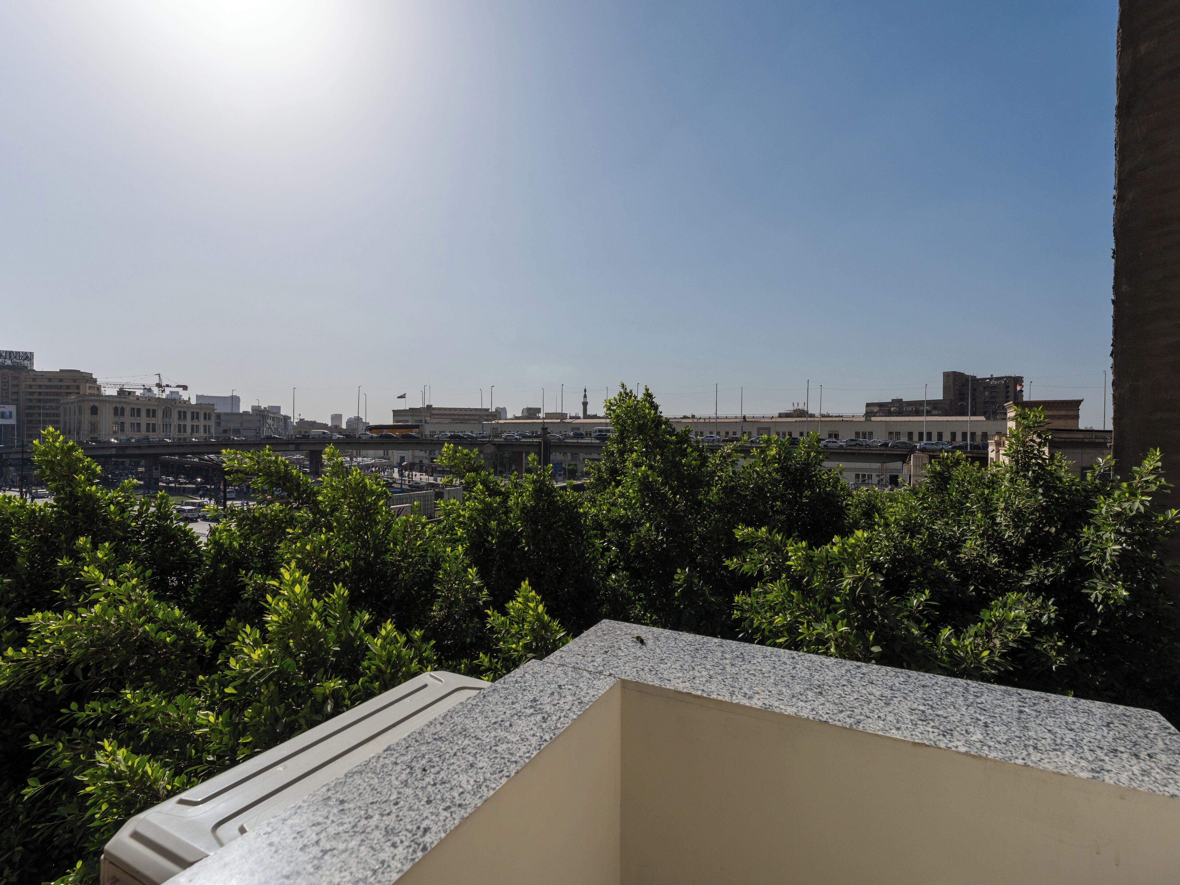 A rooftop terrace with a view of a cityscape, including buildings and a clear sky.