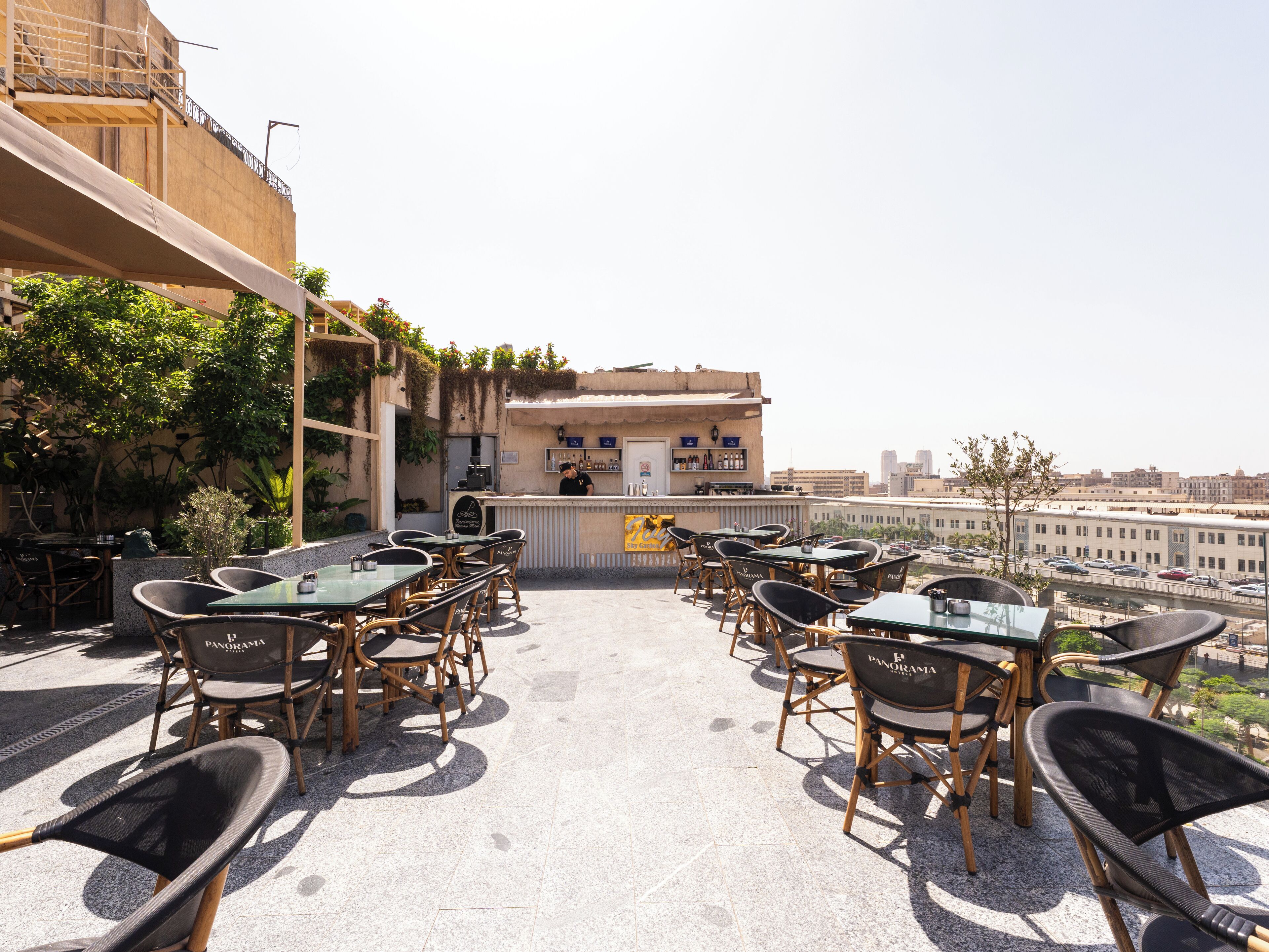 An outdoor seating area with tables and chairs, a bar, and a view of the cityscape.