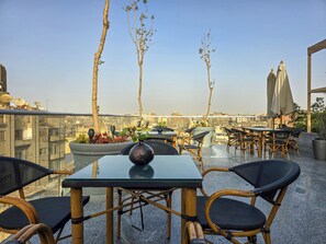 A rooftop terrace with tables and chairs, a potted plant, and a view of the cityscape. - Panorama Ramsis Hotel & Cafe (Cairo)