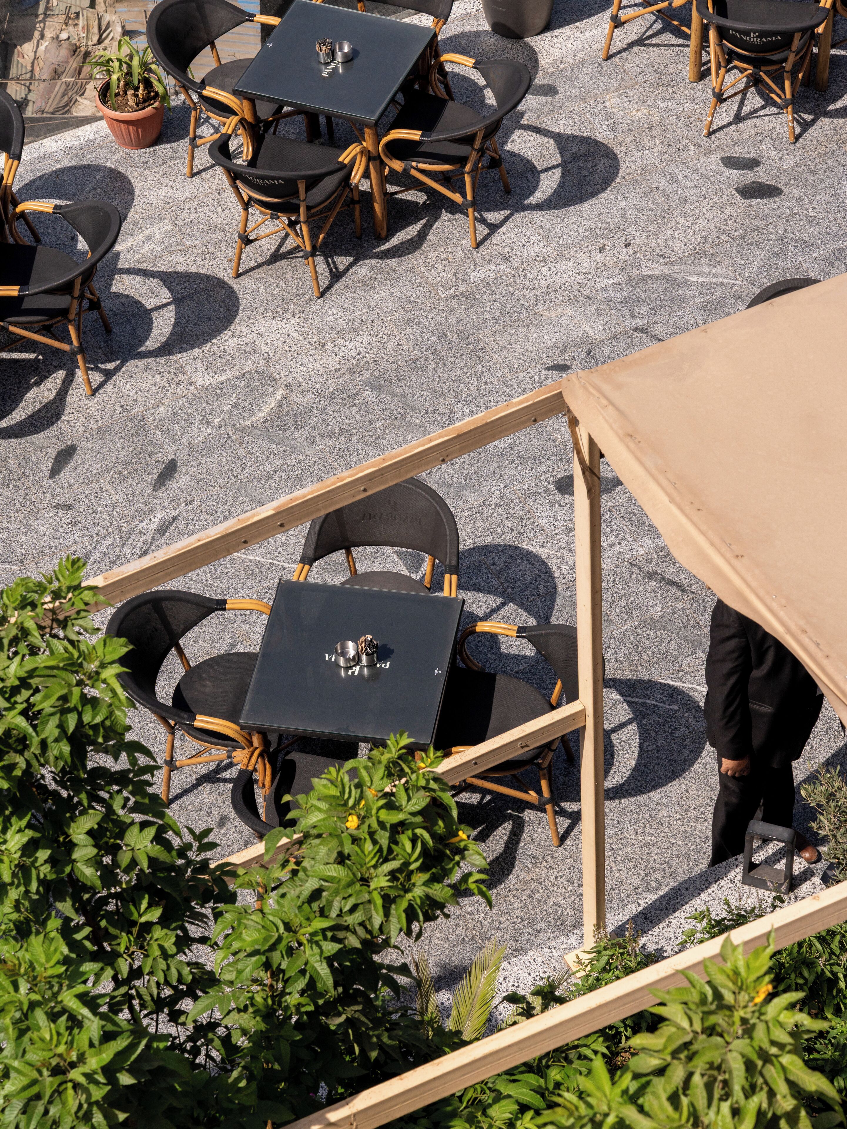 An outdoor seating area with tables and chairs, surrounded by greenery.