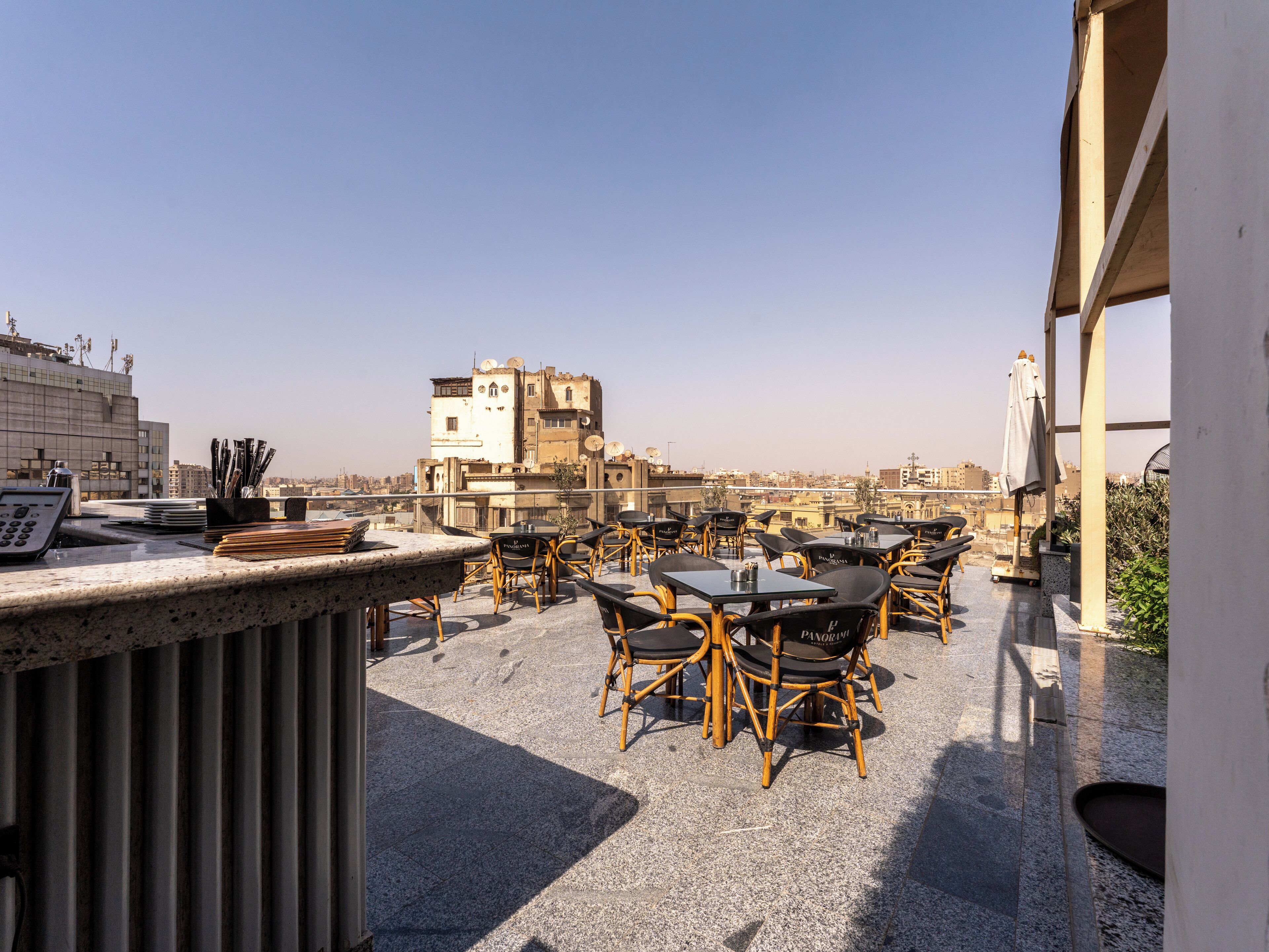 A rooftop terrace with tables and chairs, a cash register, and a view of the cityscape.