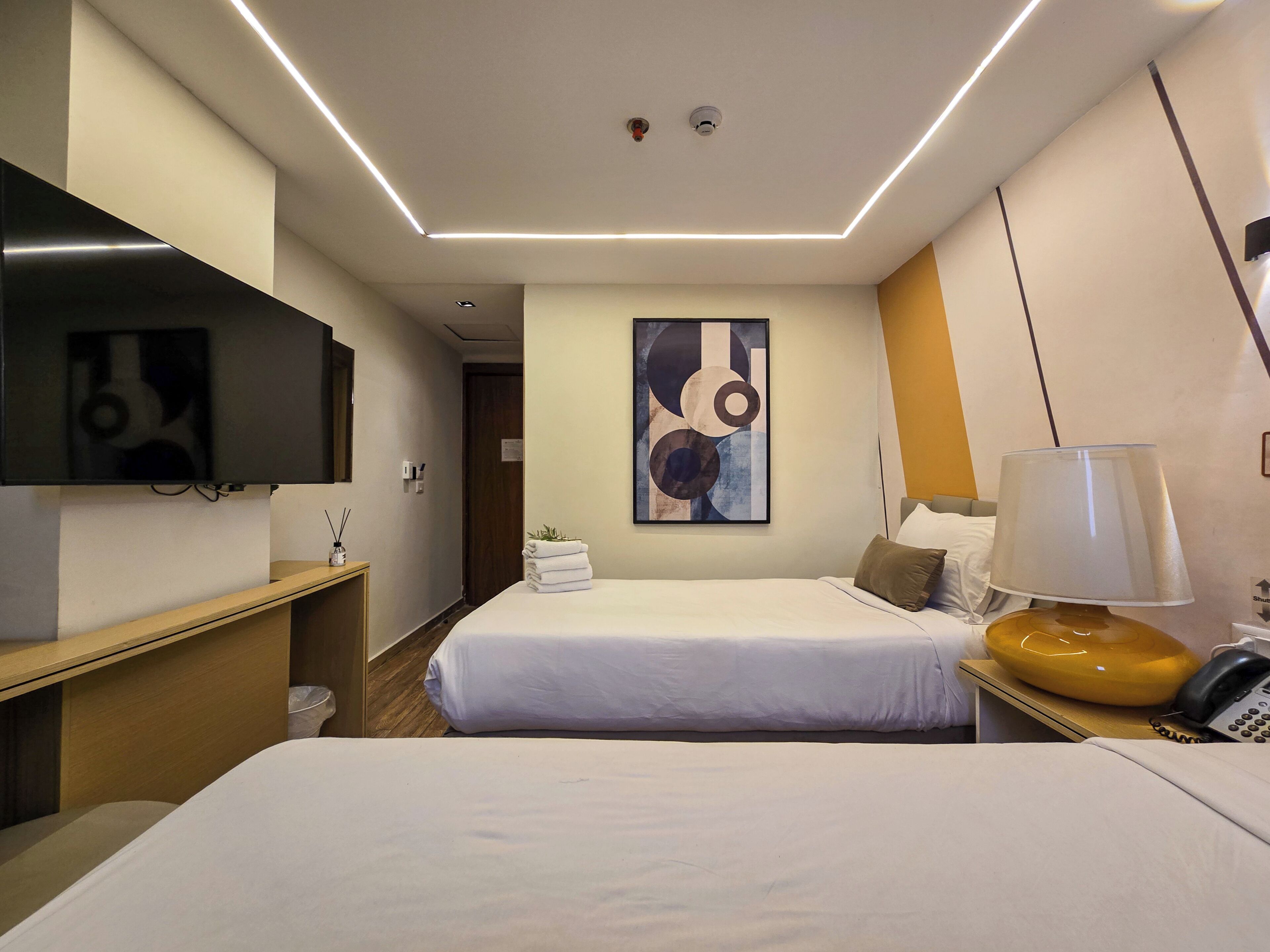 A hotel room with two beds, a TV, a painting, a lamp, and a phone on the nightstand.