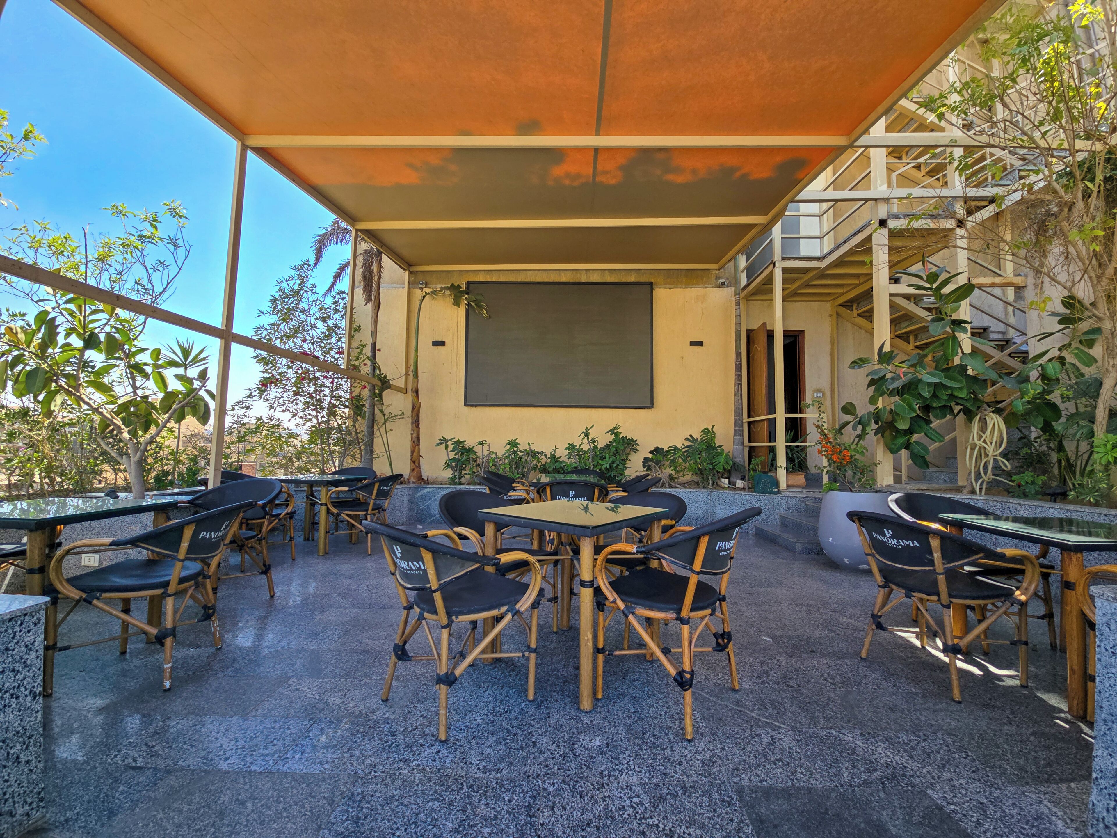 An outdoor patio with bamboo chairs and tables, a large screen, and a staircase leading to an upper level.