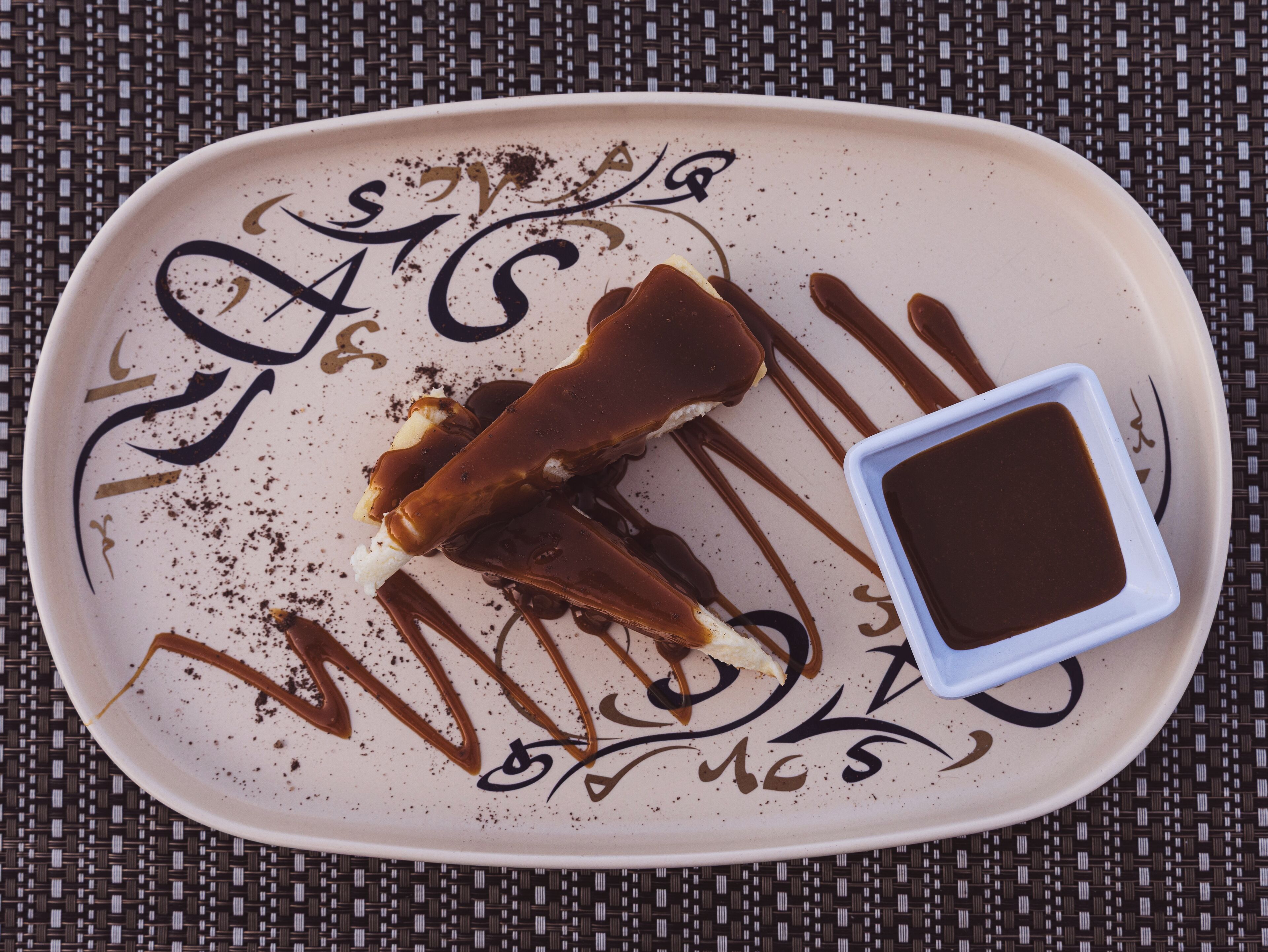 A plate with a dessert and a small dish of sauce, set on a woven mat.