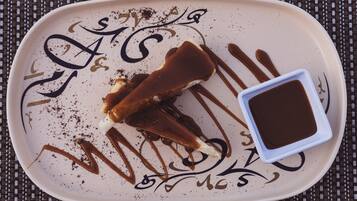 A plate with a dessert and a small dish of sauce, set on a woven mat.