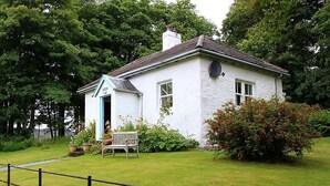 A white house with a blue door, a bench, and a garden with red flowers.