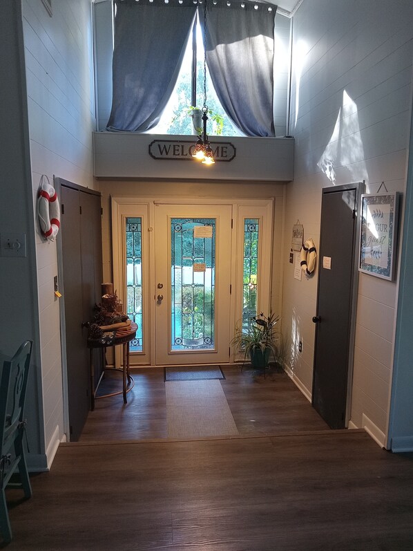 A wooden-floored entrance with a welcome sign, a life preserver, and a framed message for guests.