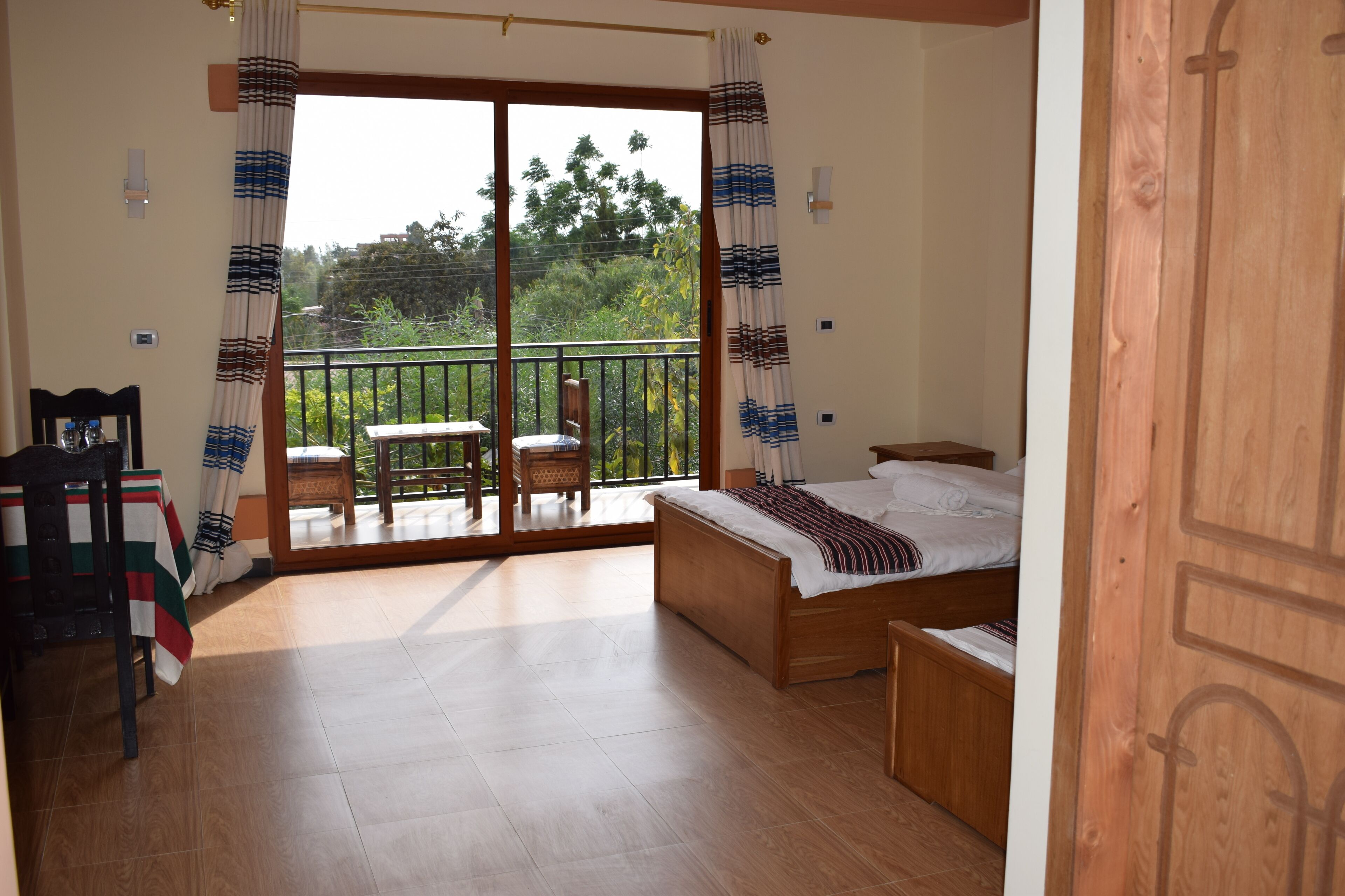 Un dormitorio con cama de madera, balcón con mesa y sillas, y vista a zonas verdes.