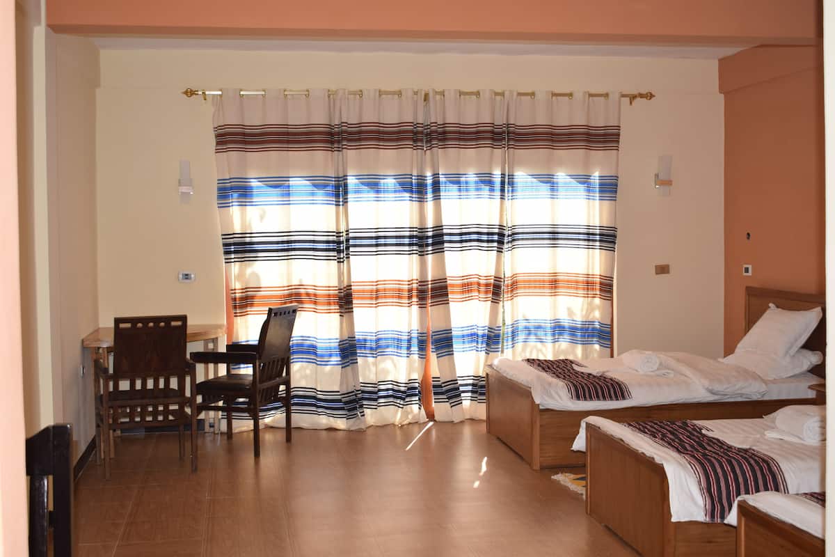 A hotel room with two beds, a wooden desk, and a chair.