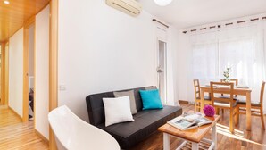 A modern living room with a black sofa, white armchair, wooden dining table, and a small wooden side table. - Barcelona Fair 5min walking. TOP 300mb WiFi (L'Hospitalet de Llobregat)