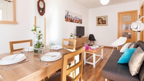A well-lit living room with a wooden dining table set for two, a black leather sofa with cushions, a television on a wooden stand, and a cityscape painting on the wall. - Barcelona Fair 5min walking. TOP 300mb WiFi (L'Hospitalet de Llobregat)