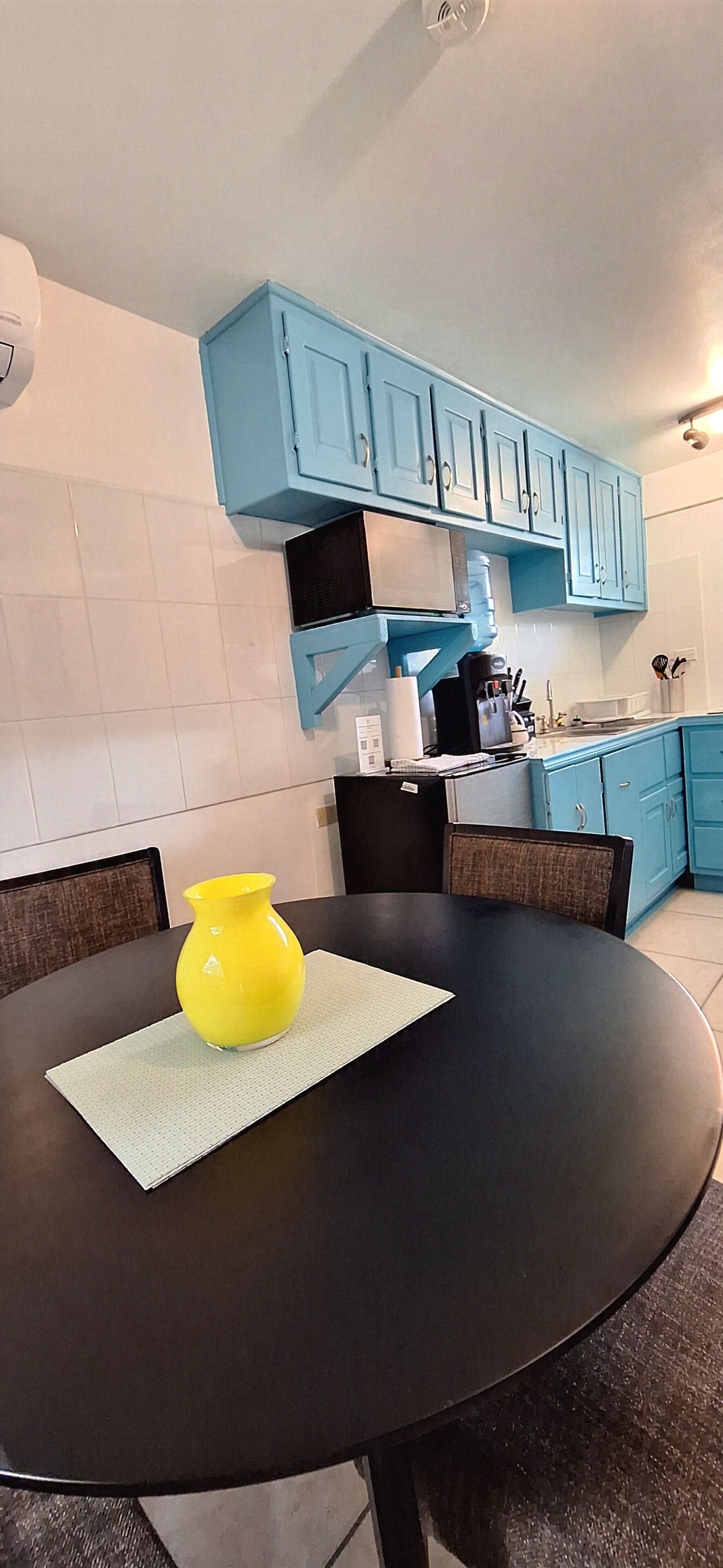 A modern kitchen with blue cabinets, a black dining table with a yellow vase, and a black chair.
