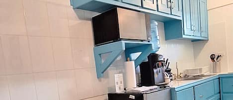 A modern kitchen with blue cabinets, a black dining table with a yellow vase, and a black chair.