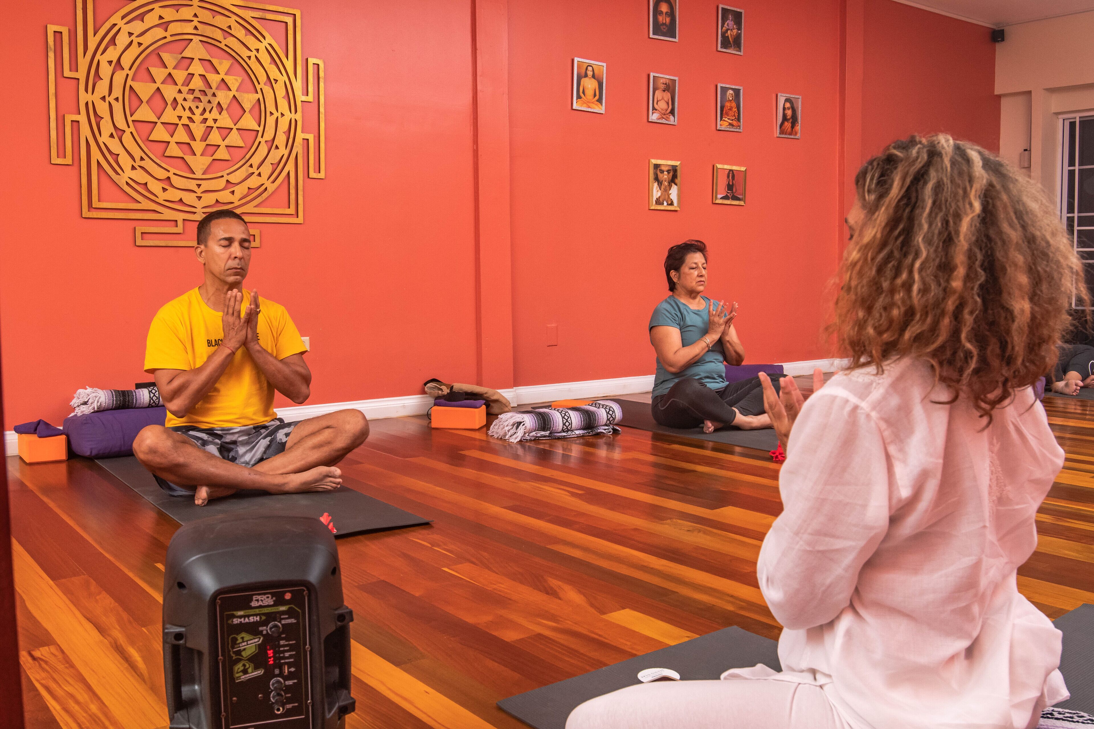A yoga class in a room with wooden flooring, red walls, and a large geometric design.