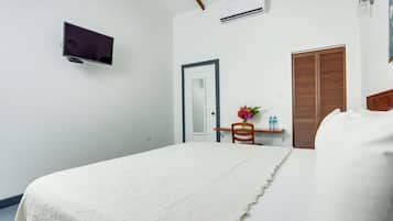 Une chambre à coucher avec un lit, un téléviseur fixé au mur, une porte en bois et une petite table sur laquelle est posé un vase de fleurs.