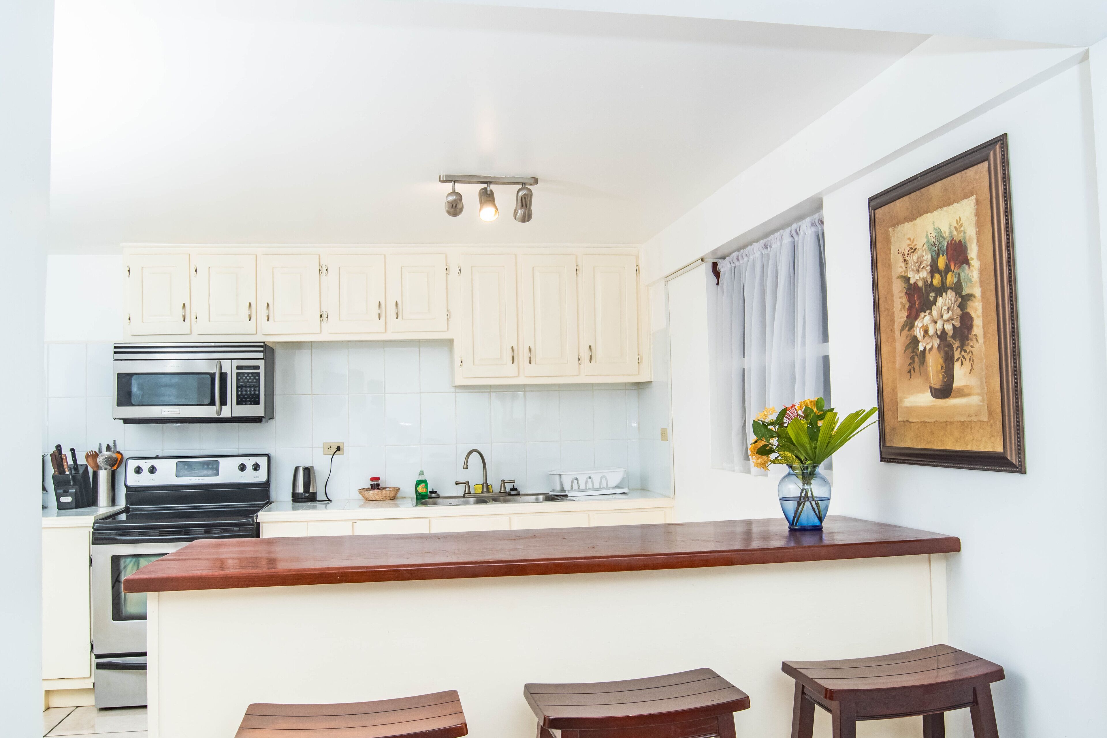 A modern kitchen with white cabinets, a central island with stools, a microwave, a stove, and a sink.