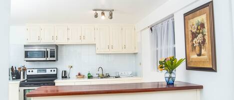 A modern kitchen with white cabinets, a central island with stools, a microwave, a stove, and a sink.