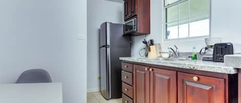 Cocina compacta con refrigerador, microondas y cafetera sobre la encimera.