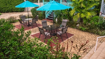 Un patio al aire libre con una mesa, sillas, dos sombrillas azules y una escalera que lleva a un porche.
