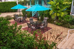Un patio al aire libre con una mesa, sillas, dos sombrillas azules y una escalera que lleva a un porche.