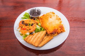 A plate with a grilled sandwich, a salad, and a small cup of sauce on a wooden table. - Harbour View Boutique Hotel & Wellness Retreat (Belize City)