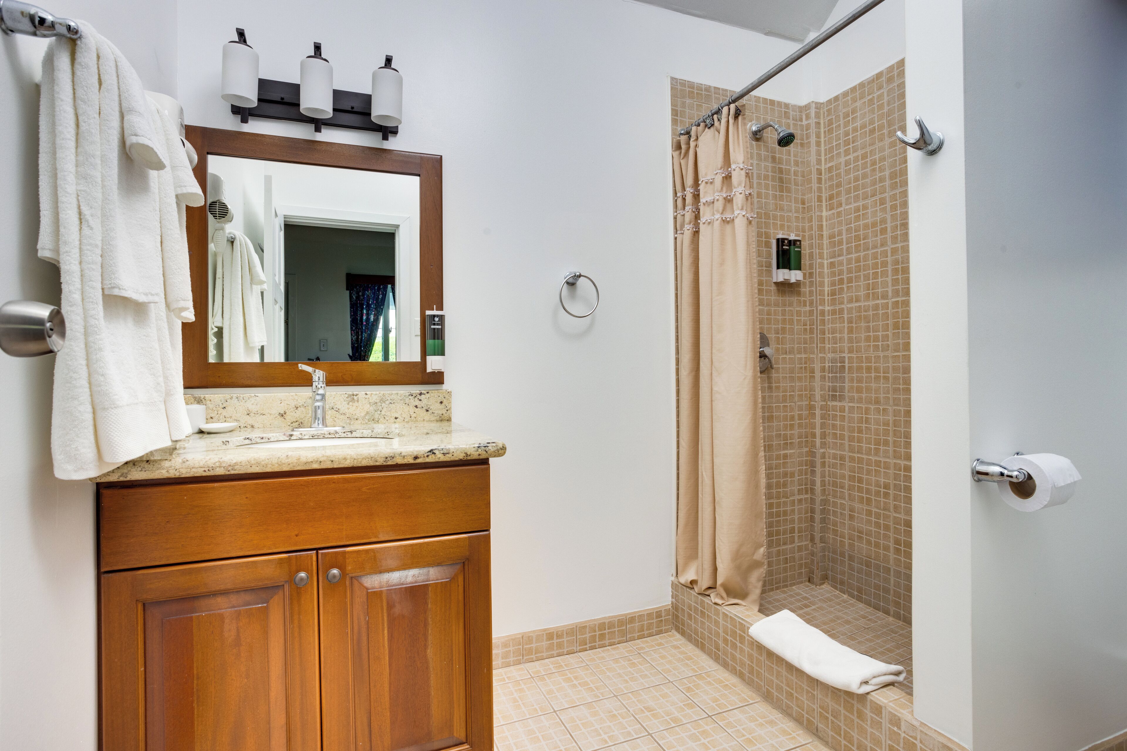 Un baño con tocador de madera, un espejo, un lavabo y zona de ducha con cortina beige.