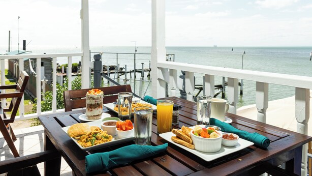 Una mesa de comedor con diversos platos y bebidas en un balcón con vistas al mar.