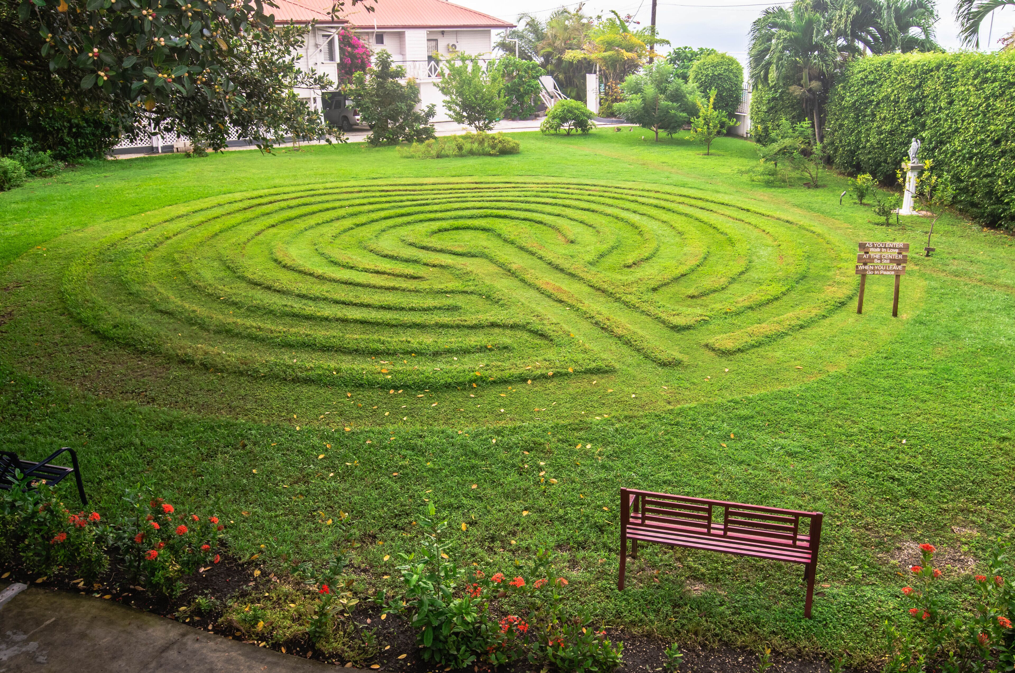 Un jardín bien cuidado con un seto laberíntico, un banco y un letrero que indica un centro de visitantes.