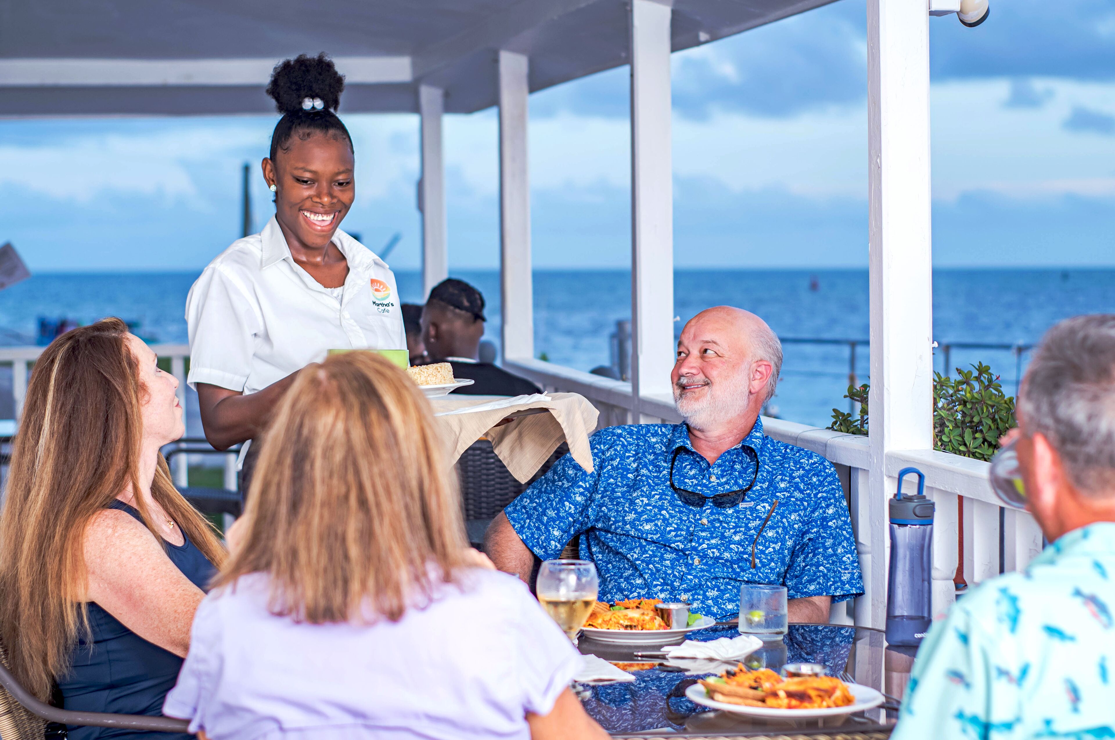 A group of people dining at an outdoor table with a view of the ocean.