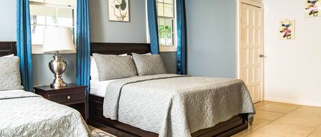 A bedroom with two beds, a nightstand, a lamp, and a window with curtains.