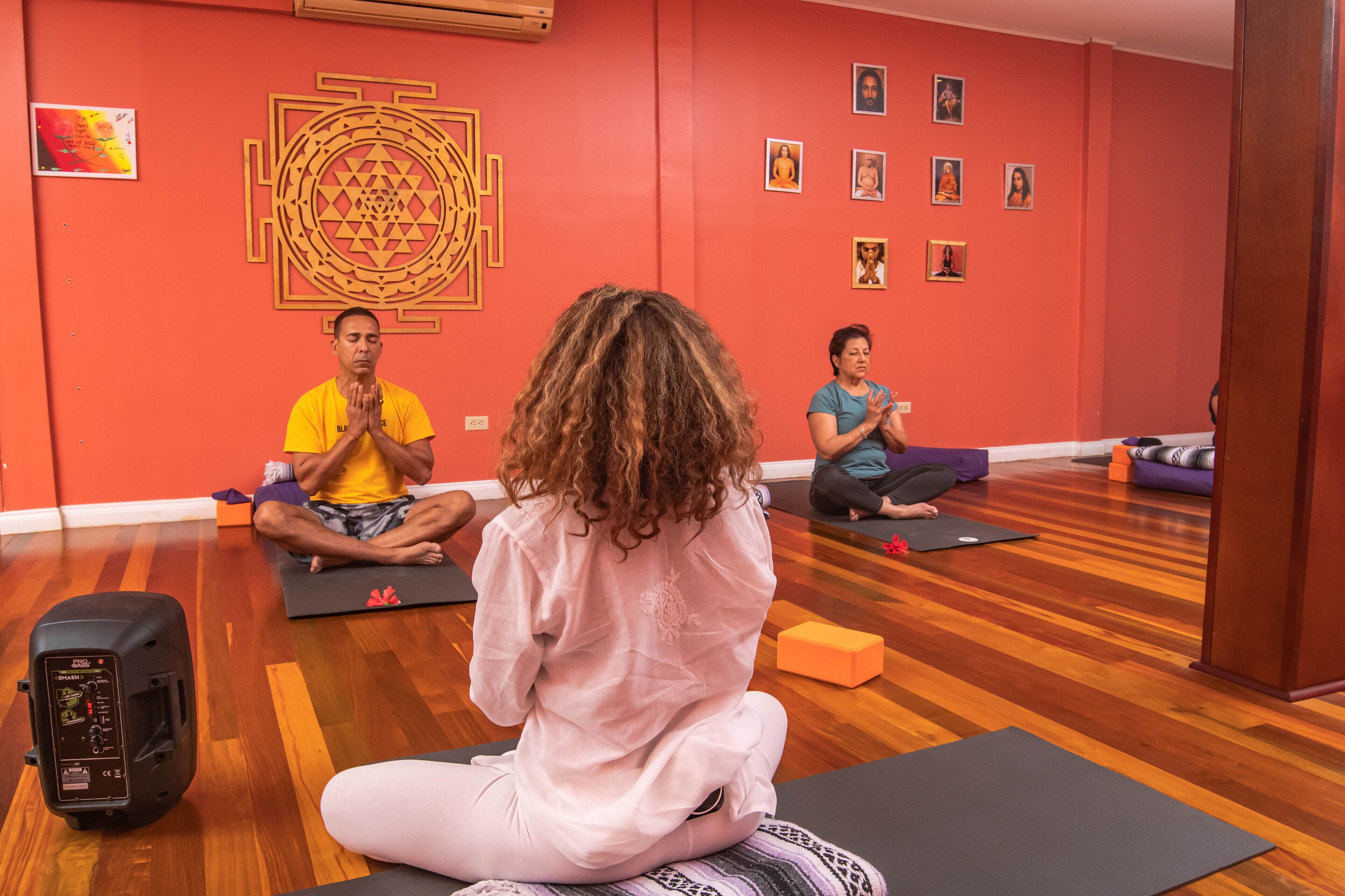 A yoga class in a room with wooden flooring, red walls, and a large geometric wall decoration.