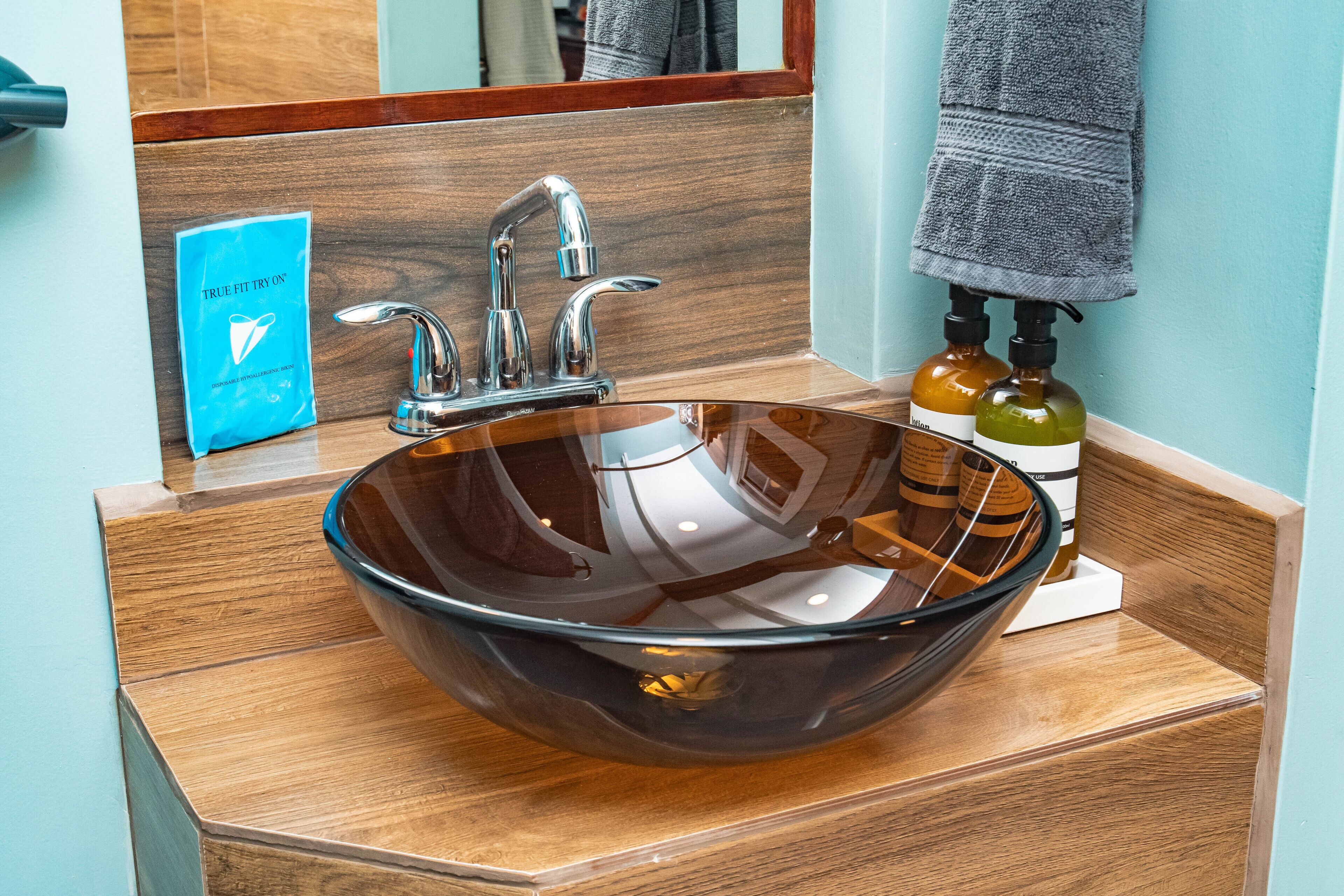 Een moderne badkamer met een grote glazen wasbak, een houten wastafelmeubel en een handdoek aan de muur.