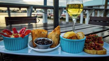 A meal with bread, dips, and a glass of white wine on a wooden table with a view of the water and boats.