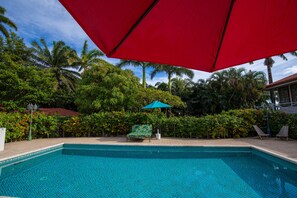 A swimming pool with a red umbrella, surrounded by lush greenery and palm trees. - Harbour View Boutique Hotel & Wellness Retreat (Belize City)