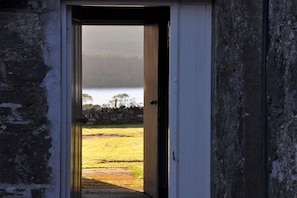A doorway leading to a grassy area with a stone wall and trees in the background.