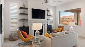 A modern living room with a sofa, two chairs, a fireplace, a television, and a large window with a desert view. - Steps to Pool | 2 Family Rooms | Resort Pool Access | Arcadia #7 (Santa Clara)