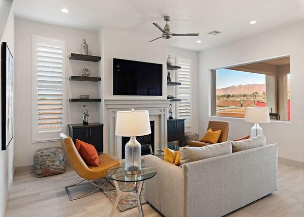 A modern living room with a sofa, two chairs, a fireplace, a television, and a large window with a desert view.