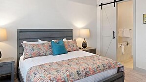 A modern bedroom with a bed, two bedside tables, a nightstand, a wardrobe, and a bathroom visible through an open door. - Steps to Pool | 2 Family Rooms | Resort Pool Access | Arcadia #7 (Santa Clara)