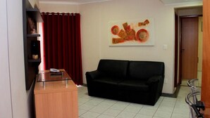 A living room with a black sofa, a wooden cabinet, a red curtain, and a wall-mounted abstract painting. - Thermas Paradise (Rio Quente)