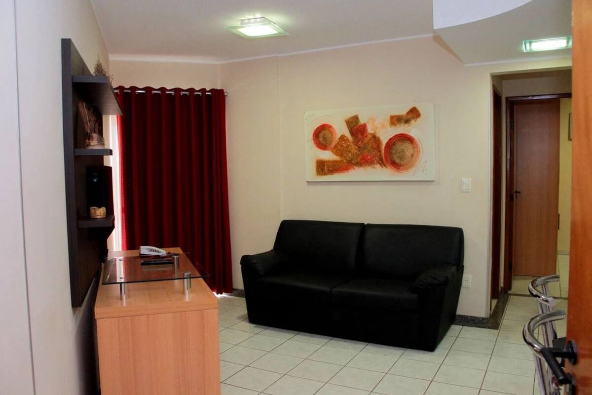 A living room with a black sofa, a wooden cabinet, a red curtain, and a wall-mounted abstract painting.