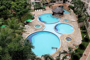 Un área de piscina con múltiples niveles, varias piscinas y jacuzzis, rodeada de palmeras y sillas de descanso.