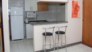 A compact kitchen with white cabinets, a built-in microwave, a stainless steel sink, and two bar stools. - Thermas Paradise (Rio Quente)