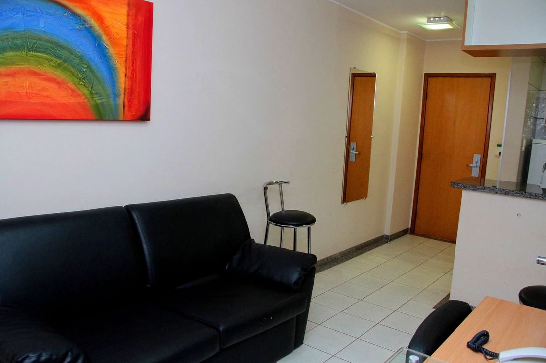 A room with a black leather sofa, a small table with a telephone, and a painting on the wall.