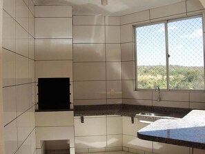 A kitchen with white tiles, a window with a view, and a granite countertop. - Thermas Paradise (Rio Quente)