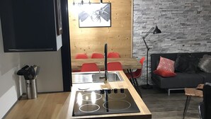 Une cuisine compacte avec un lave-linge intégré, un coin repas avec des chaises rouges et un canapé gris.