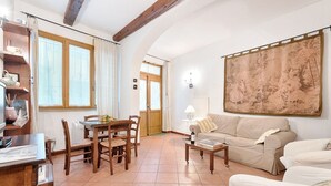 Un salon comprenant une table à manger en bois, des chaises, un canapé, une table basse et une grande tapisserie accrochée au mur.